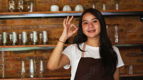 Young Asian woman barista wear apron OK gesture