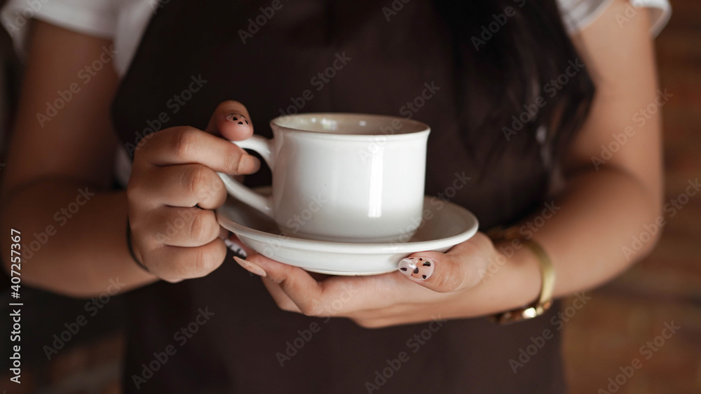 Asian Women Barista smiling and looking to camera in coffee shop counter. Barista female holding coffee cup at cafe Asian Women Barista smiling and looking to camera in coffee shop counter. Barista female holding coffee cup at cafe