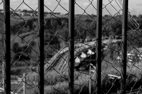 Railing and metellic net in the foreground, in the background, out of focus rails of an urban train. Black and white photo photo