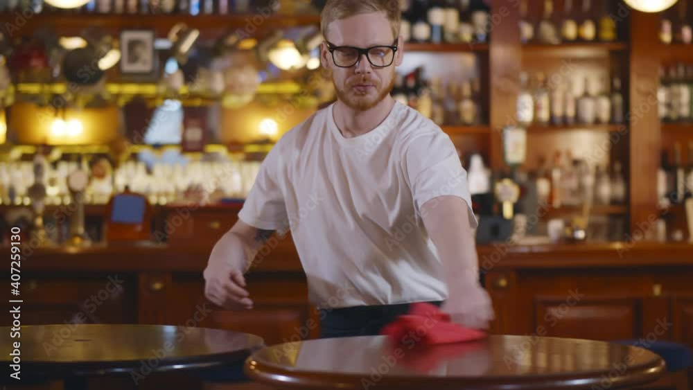 Young waiter in workwear wiping table with duster preparing for new guests Young waiter in workwear wiping table with duster preparing for new guests
