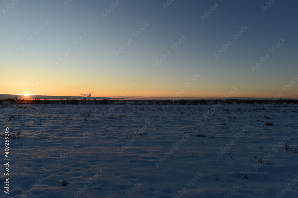 Sunset in the blue clear frost sky over a snowy field
