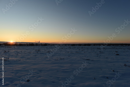 Sunset in the blue clear frost sky over a snowy field