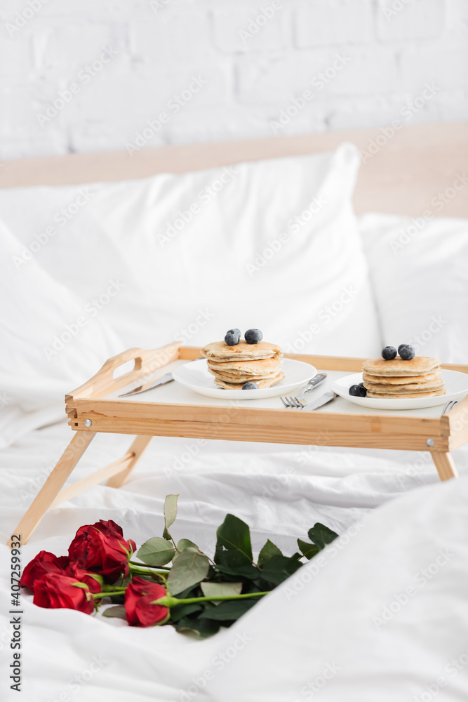 wooden tray with delicious pancakes and blueberry near red roses on white bedding, valentines day concept - obrazy, fototapety, plakaty 