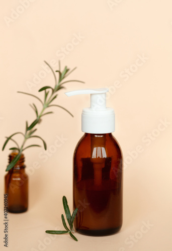 Brown glass bottle with a pump of cosmetic products framed by green leaf branches  beige background. Natural organic spa cosmetic beauty concept. Front view Mock up.