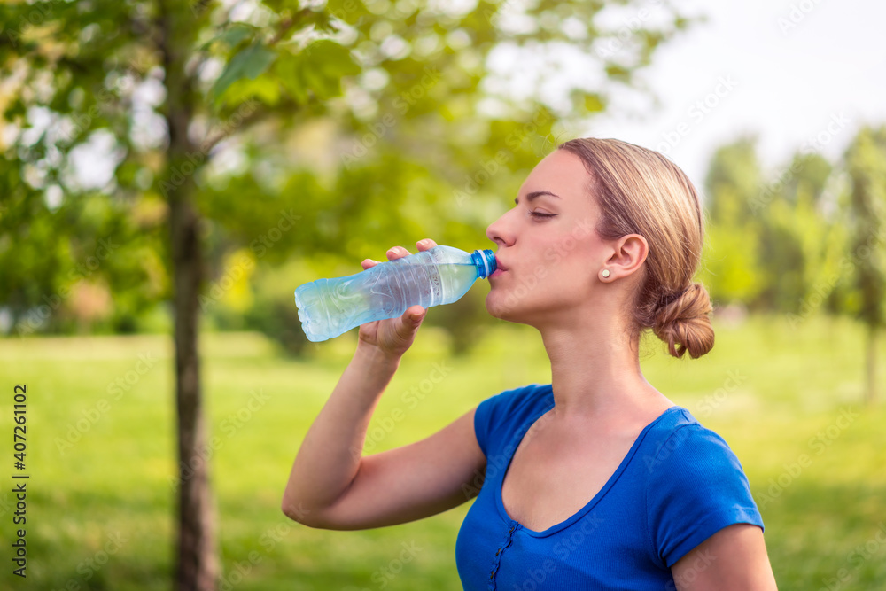 Young beautiful women resting and drinking water after doing exercises in park Young beautiful women resting and drinking water after doing exercises in park