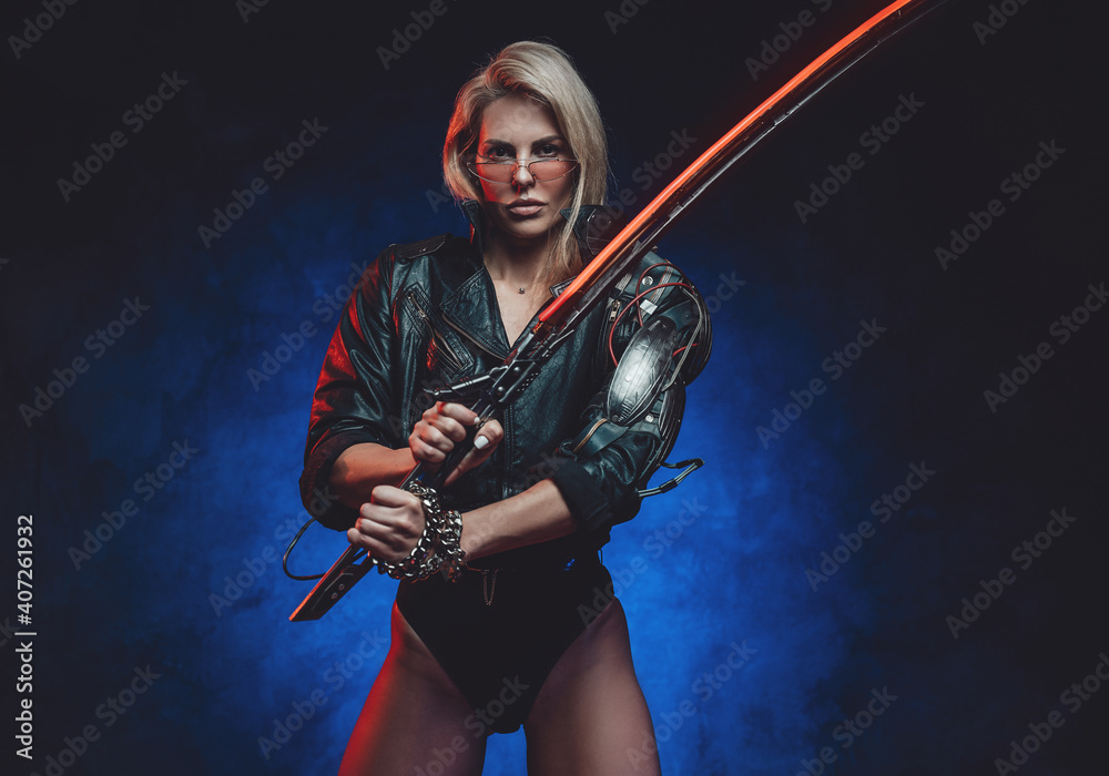 Caucasian woman in cyberpunk style poses in blue background with glowing sword looking at camera.