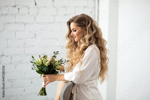 Beautiful bride in a peignoir with a wedding bouquet in profile