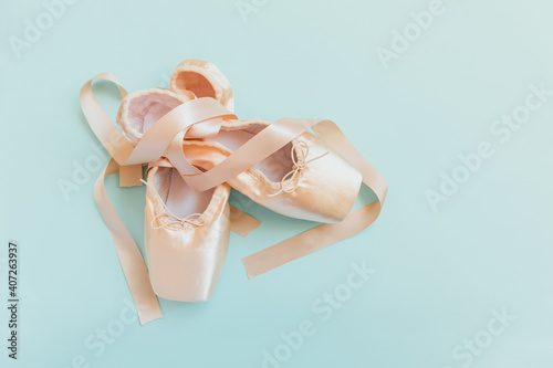 New pastel beige ballet shoes with satin ribbon isolated on blue background. Ballerina classical pointe shoes for dance training. Ballet school concept. Top view flat lay, copy space photo