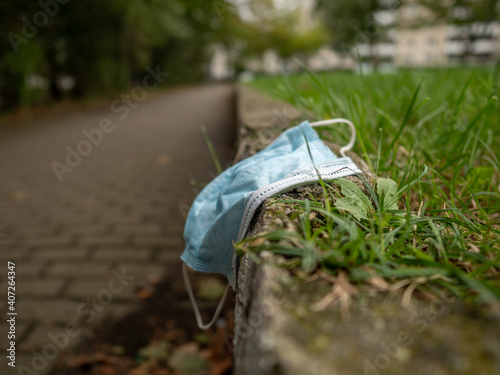Used face mask next to a sidewalk in an urban area as environmental pollution in a public park plastic waste junk