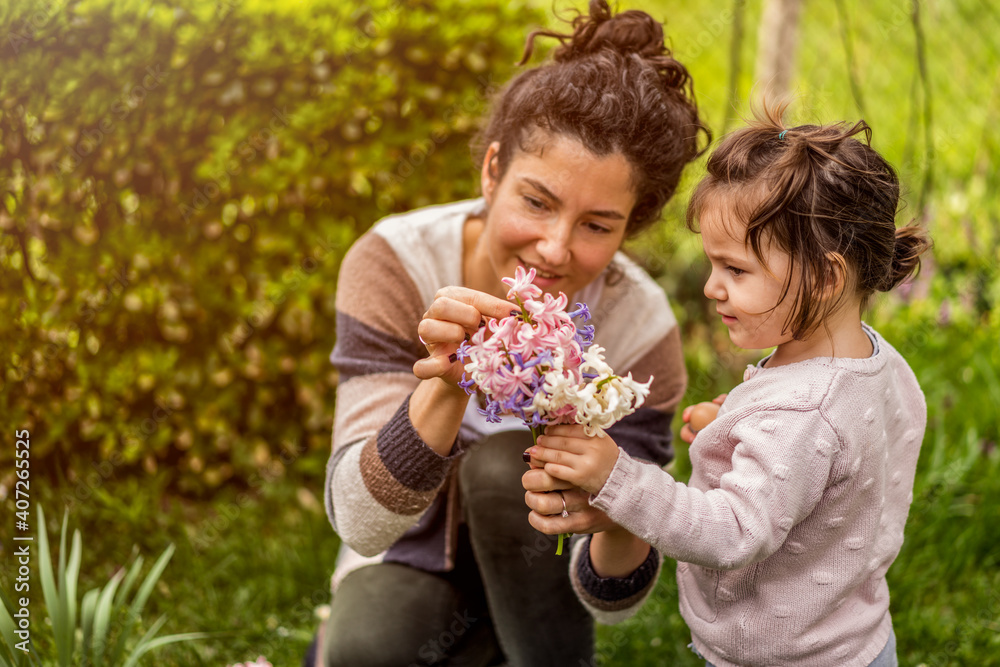 Young beautiful mother and cute little daughter in the garden with flowers Young beautiful mother and cute little daughter in the garden with flowers