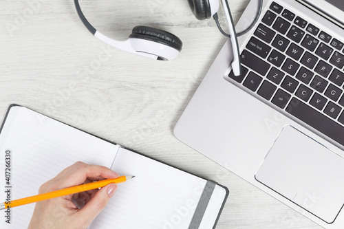 Laptop. keyboard and headphones on grey wooden desk. hand with pencil and notebook. Helpdesk or call center headset. Distant learning or working from home, online courses or support center concept.