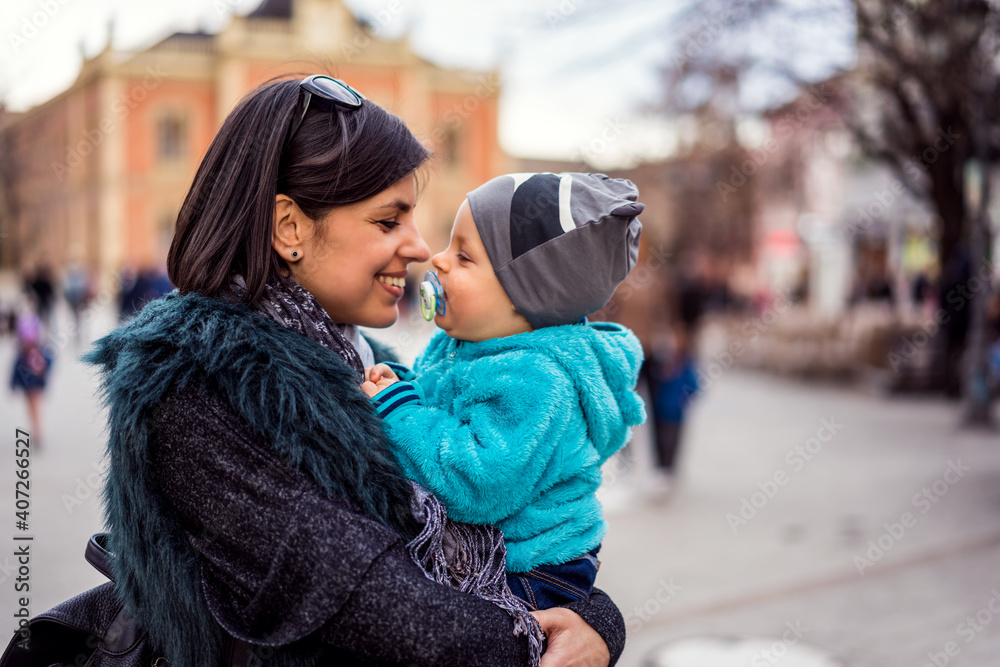 Gorgeous mom cuddling happy baby boy outdoors