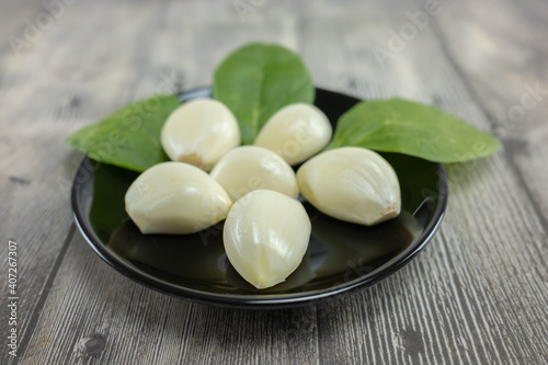 Heads of peeled garlic and green leaves on a plate