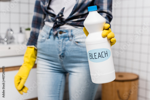 Bottle with bleach lettering in hand of woman in rubber glove on blurred background in bathroom photo
