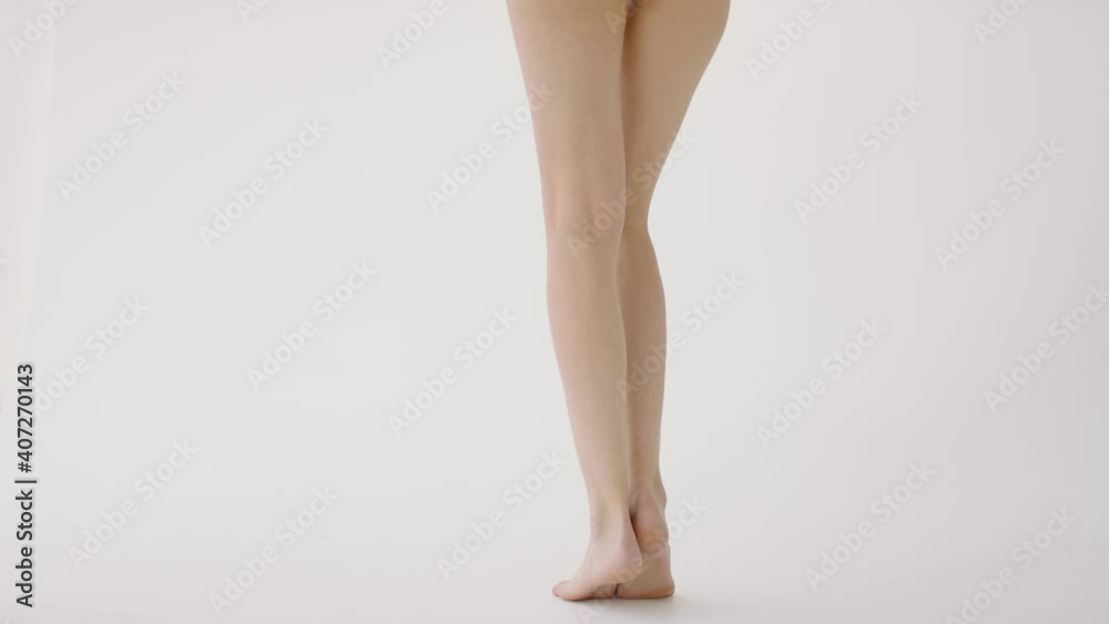 Female legs close up. Back view. Slender young woman stands on tiptoe on white background. Concept of skin care, cosmetology, cosmetics Female legs close up. Back view. Slender young woman stands on tiptoe on white background. Concept of skin care, cosmetology, cosmetics