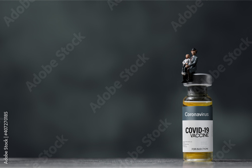 Seniorman and son (figurine) sitting on Coronavirus COVID-19 vaccine vial.Healthcare And Medical concept background. photo