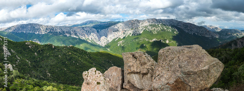 wide panoramic landscape of Supramonte Mountains with limestone rock, green forest, mediterranean vegetation and view of Gola Su Gorropu gorge, Nuoro, Sardinia, Italy. Summer cloudy day photo