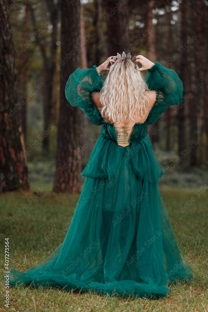 young beautiful blonde hair woman queen. Princess walks. autumn green forest mystic. Vintage medieval shiny crown. Long evening green dress. magic fantasy. back view