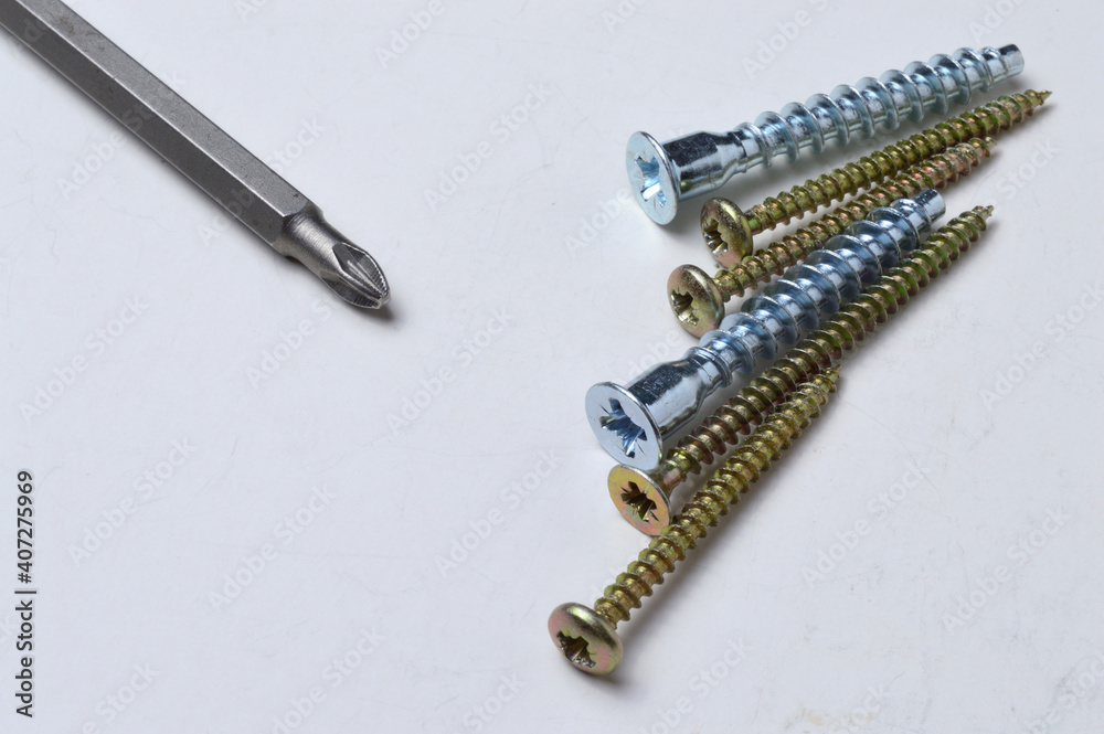 several screws and a bit from a screwdriver lie on a light background. close-up. several screws and a bit from a screwdriver lie on a light background. close-up.