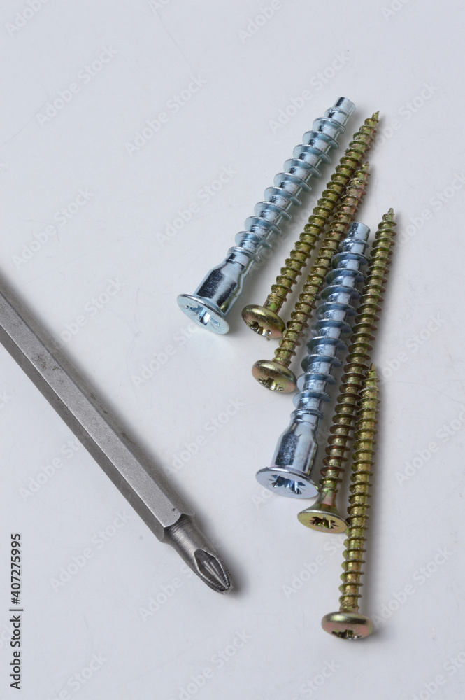 several screws and a bit from a screwdriver lie on a light background. close-up. several screws and a bit from a screwdriver lie on a light background. close-up.