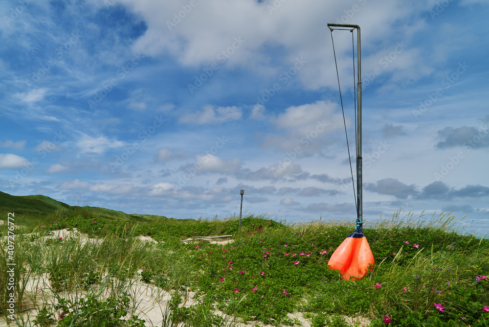 Orange ball attached to a rope at the bottom of a pole standing in the dunes of Nymindegab, Denmark - it can be pulled up and then serves as a sign that the army is doing an exercise here