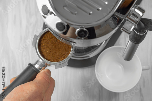 The process of making a delicious and aromatic drink for a coffee break. Top view of a hand holding a portafilter of a coffee machine filled with ground coffee to make an espresso.