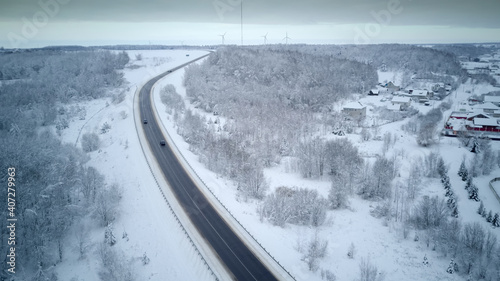View from the drone on the paved road, cars, winter snow-covered forest, village. Beautiful winter landscape with paved road © yaroslav1986