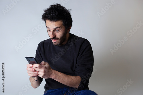 White Argentinian adult bearded man using smartphone social media with surprised expression on a white background with copy space.