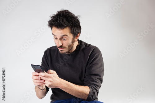 White Argentinian adult bearded man using smartphone social media with surprised expression on a white background with copy space. © Moha