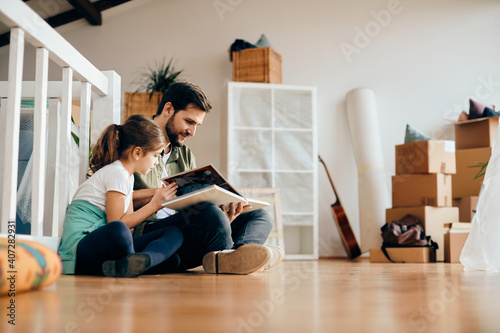 Happy father and daughter looking at family photo album at their new apartment.