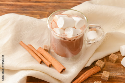 Tasty cocoa with cinnamon and marshmallows in cup on wooden background