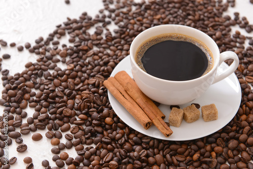 Tasty coffee with cinnamon and beans in cup on light background