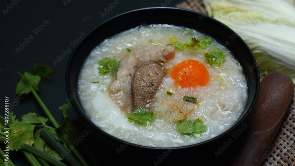 rice porridge, rice gruel or congee with pork, egg, sliced ginger and vegetable, delicious the traditional Chinese breakfast. on a dark background.