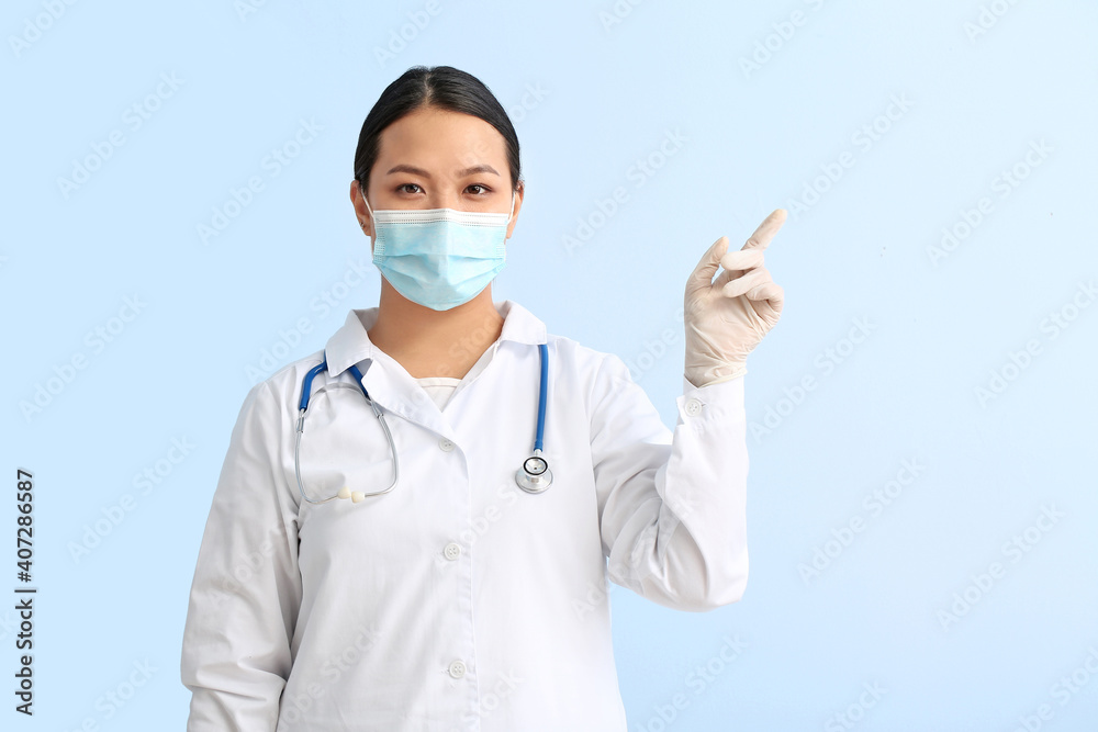 Portrait of female Asian doctor pointing at something on color background Portrait of female Asian doctor pointing at something on color background