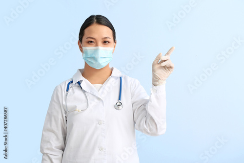 Portrait of female Asian doctor pointing at something on color background