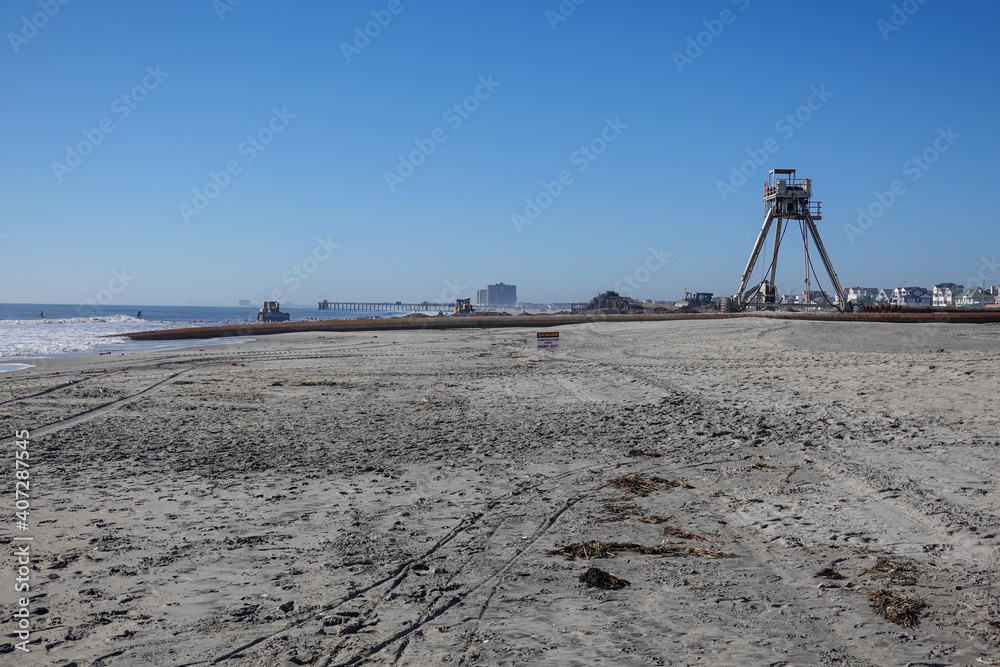 An amphibious buggy tower used in a beach replenishment operation near a large pipe on a long sandy beach An amphibious buggy tower used in a beach replenishment operation near a large pipe on a long sandy beach