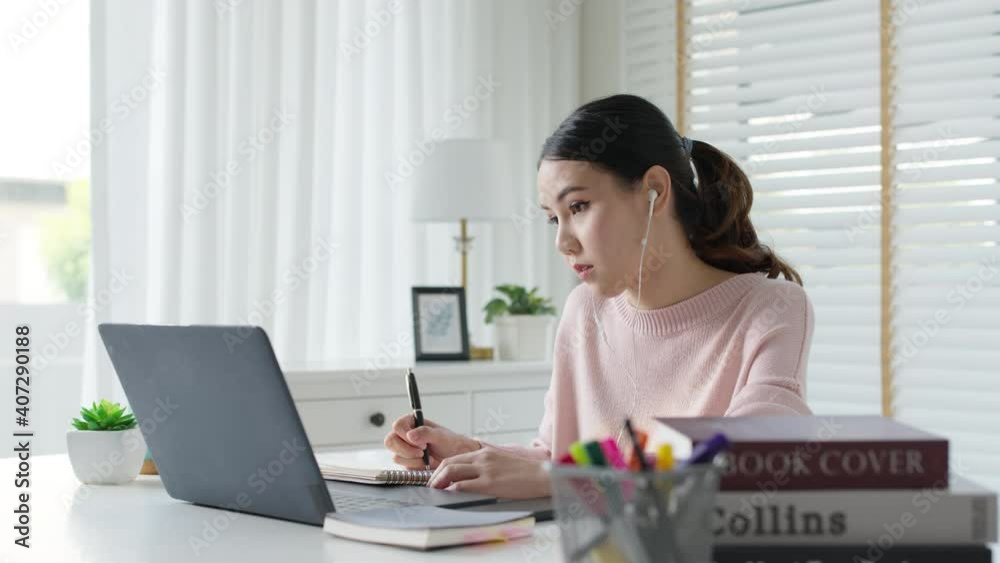Candid young attractive asian female employee wear earphone listen to digital online course development program in quarantine social distance at home reskill upskill school class for career path.
