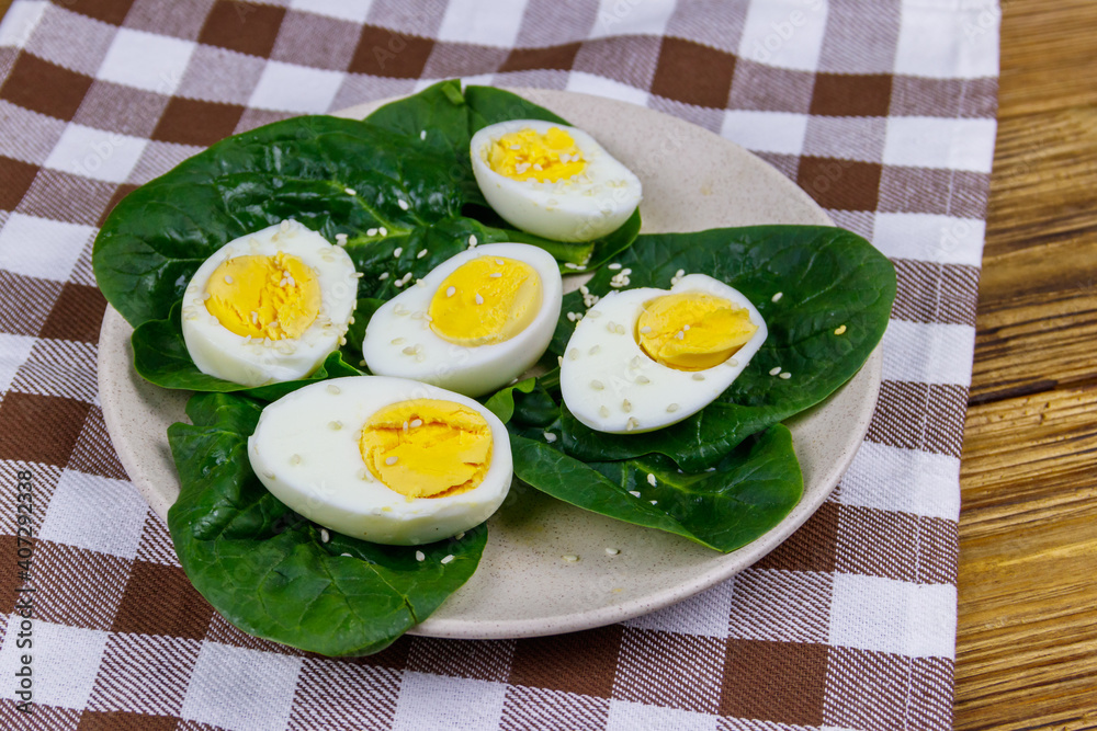 Boiled eggs with fresh spinach leaves and sesame seeds on wooden table Boiled eggs with fresh spinach leaves and sesame seeds on wooden table