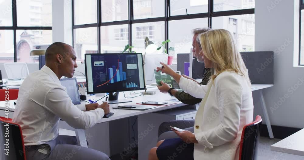 Diverse business people sitting using computer and takling at desk in office