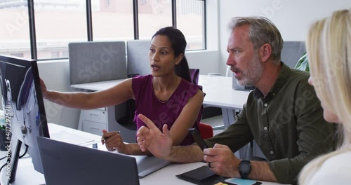 Diverse business colleagues sitting at desk using computer and dicsussing in office photo