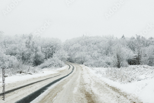 A snow-covered road through a snow-white forest covered with snow on a frosty day.