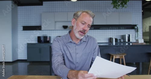 Caucasian businessman having video chat going through paperwork in office kitchen photo