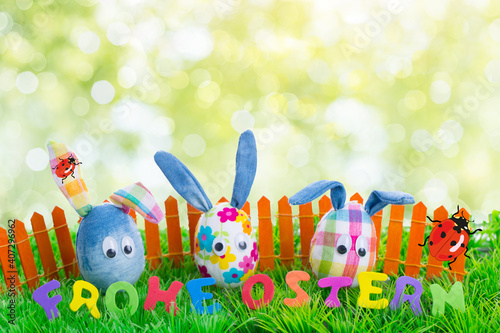 Cute 3 easter eggs as decorated easter bunnies in front of green fresh spring background in nature with colorful fence and fresh background.