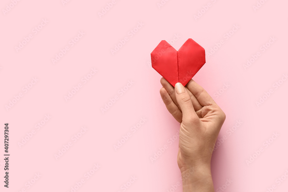 Hand with origami heart on color background