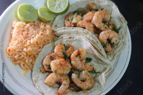 Shrimp tacos with rice soup complement and some lemons on a white plate.