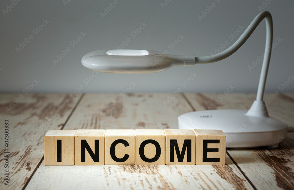 © Superzoom - A table lamp illuminates wooden blocks with the word INCOME