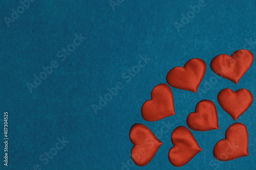 Red textile hearts in corner on blue cardboard background. Valentines Day concept, copy space, flat lay.