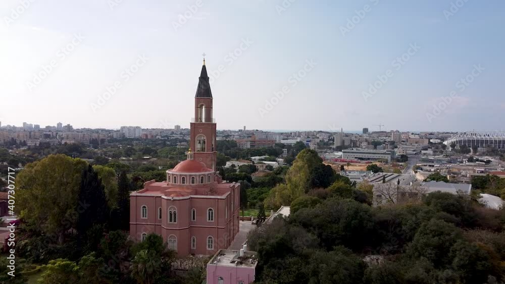 Aerial forward shot of a pink church surrounded by trees, in front of city buildings and blue sky, on a sunny day. Aerial forward shot of a pink church surrounded by trees, in front of city buildings and blue sky, on a sunny day.