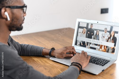 Картината върху платно An African-American guy looks through job search sites, work vacancies on the laptop, a multiracial jobless seeker looking for new position or part-time job on website page