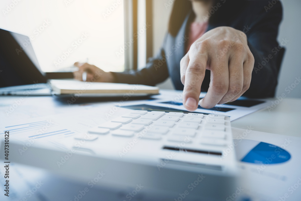 Businesswomen bookkeeper hand use calculator and laptop doing account for paying tax on white desk in working office Businesswomen bookkeeper hand use calculator and laptop doing account for paying tax on white desk in working office